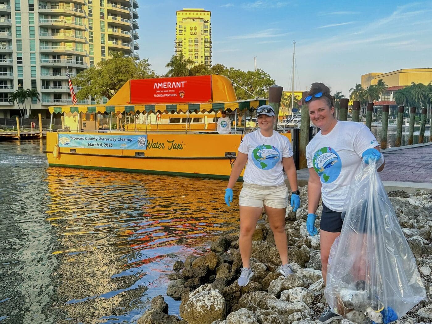 2 girls cleaning up debris in fort lauderdale with amerant bank advertisement in background.
