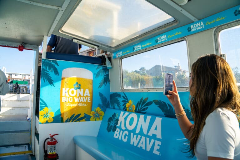 Girl photographing Kona Big wave outdoor advertisement on the fire island ferry