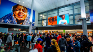 A static Nike advertisement at Whitehall Terminal featuring two images: one of a tired female runner post-race, and another of a runner pushing through during the marathon. The digital ad reads "This was amazing," celebrating resilience and the beauty in the struggle.